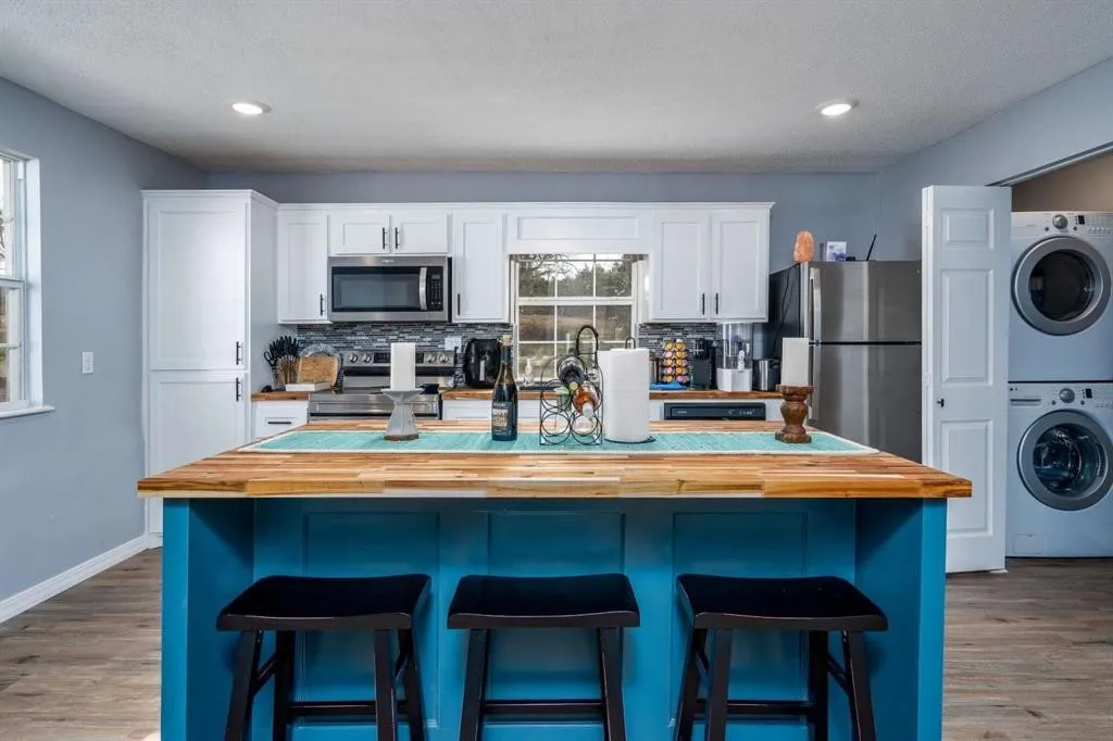 Kitchen featuring a central island with wood countertop, white cabinetry with dark hardware, stainless steel appliances, and wood-finish flooring