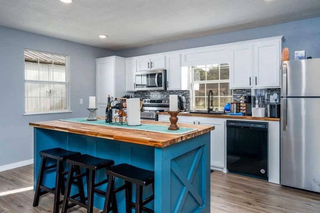 Kitchen featuring a blue-painted island with a wood-finish countertop, white cabinetry with dark hardware, a mosaic tile backsplash, and stainless steel appliances