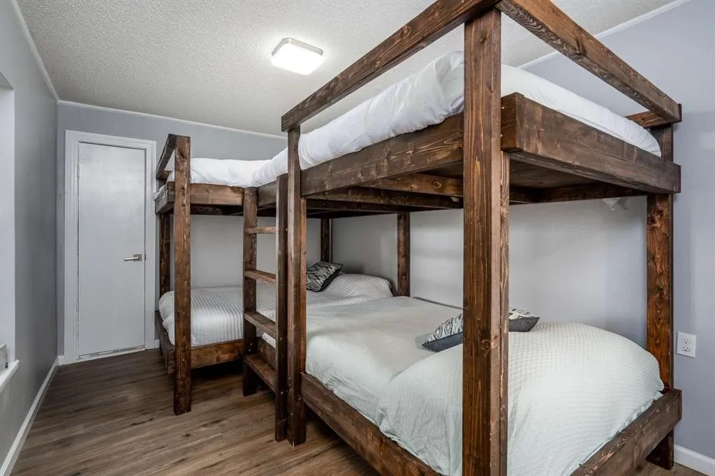 Room with two wooden bunk beds, wood-finish flooring, light gray walls, and a ceiling-mounted light fixture