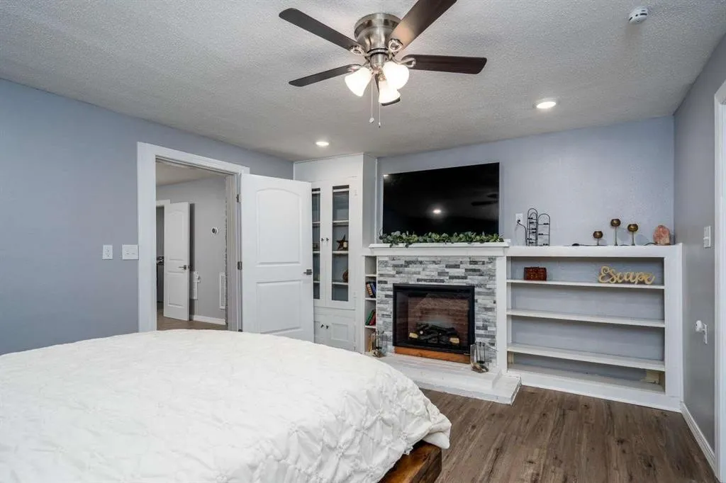 Fireplace with stone surround, wood-finish flooring, built-in shelving, recessed lighting, and a ceiling fan