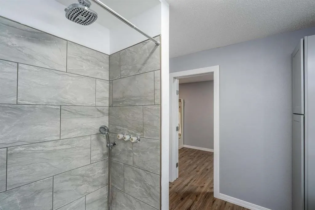 Shower with large format gray tile and rainfall showerhead, complemented by light gray walls and wood-finish flooring