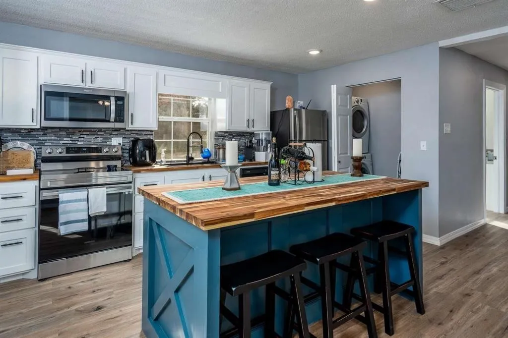 Kitchen featuring a central island with wood-finish countertop, white cabinetry with dark hardware, stainless steel appliances, and wood-finish flooring