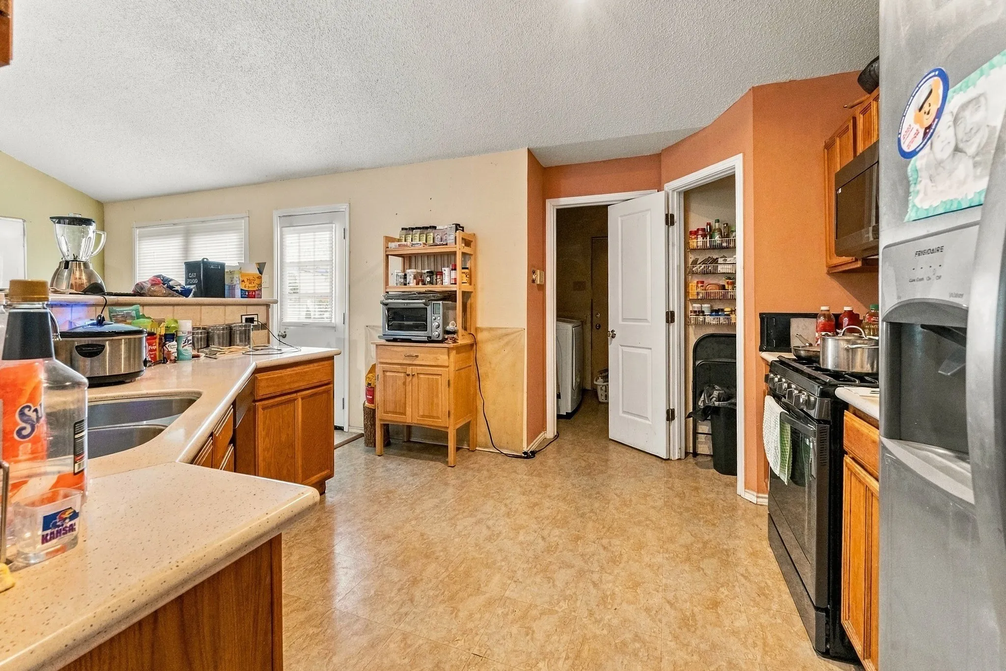 Kitchen featuring a stainless steel refrigerator, black range, wood-finish cabinetry, and light-colored countertops