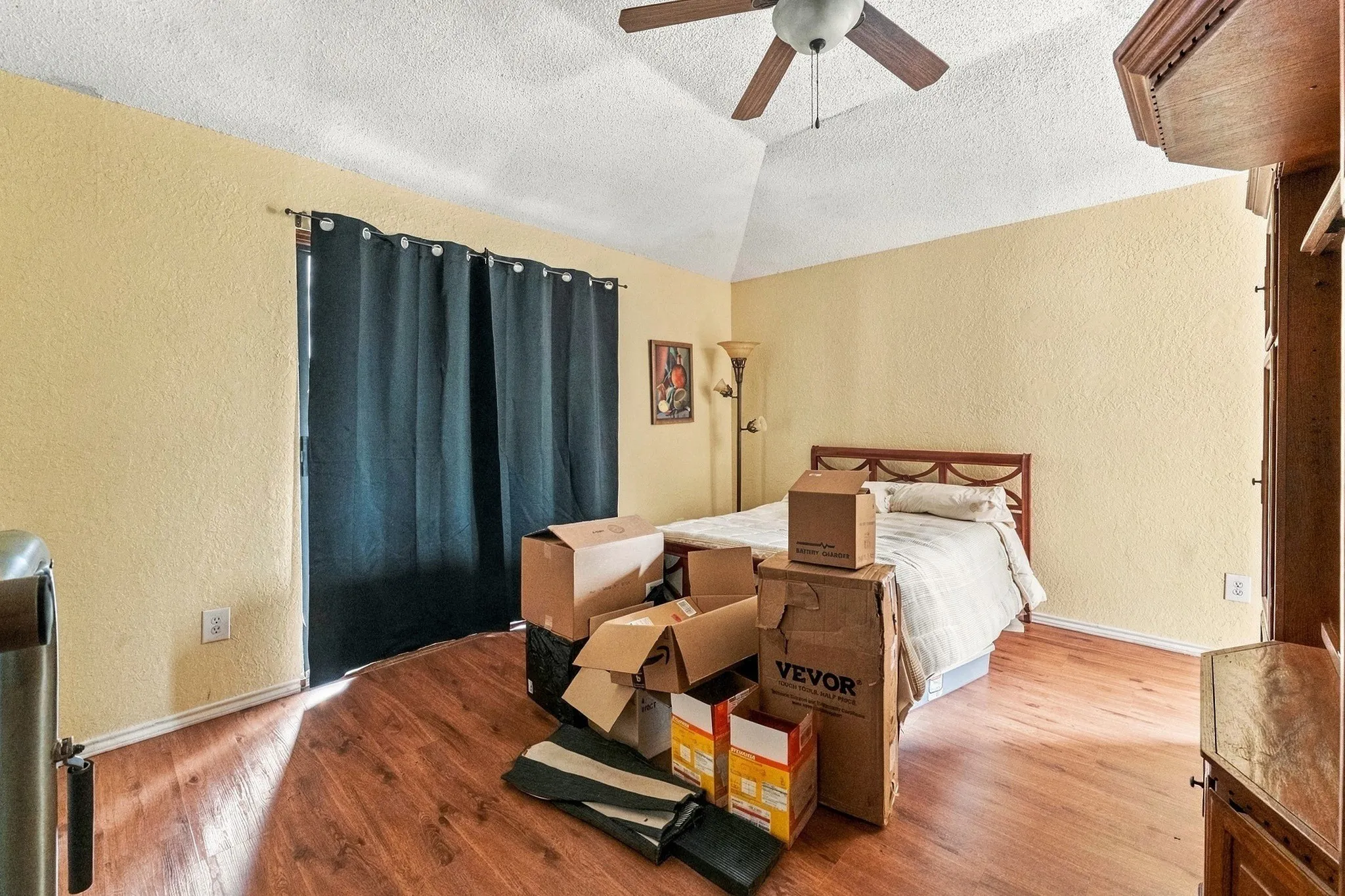 Vaulted ceiling with a ceiling fan, wood-finish flooring, and a window with dark curtains