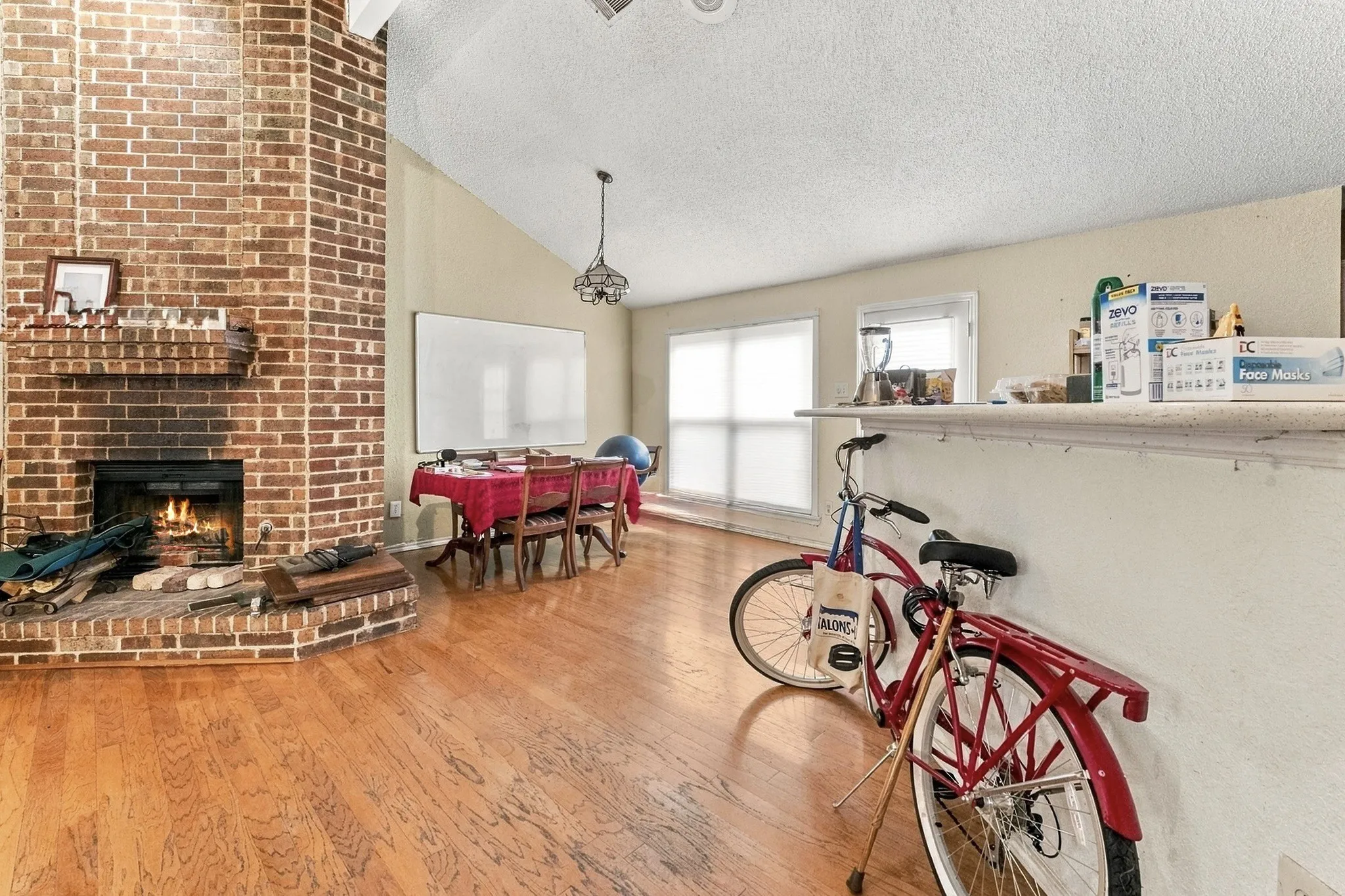 Brick-faced fireplace with hearth, wood-finish flooring, vaulted ceiling, and built-in counter