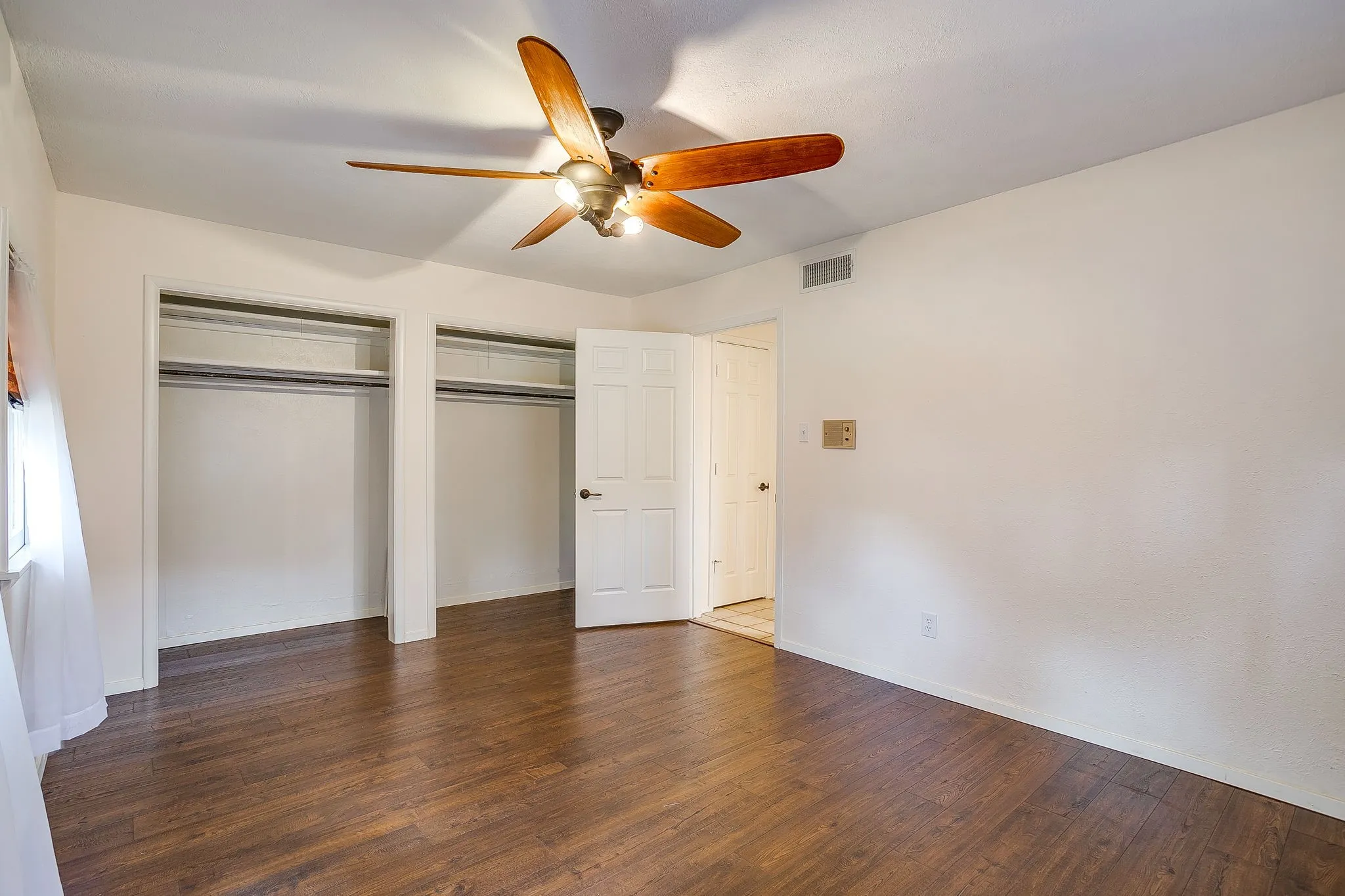 Wood-finish flooring, ceiling fan with integrated lighting, two built-in closets with shelving and hanging rods, and a white paneled door