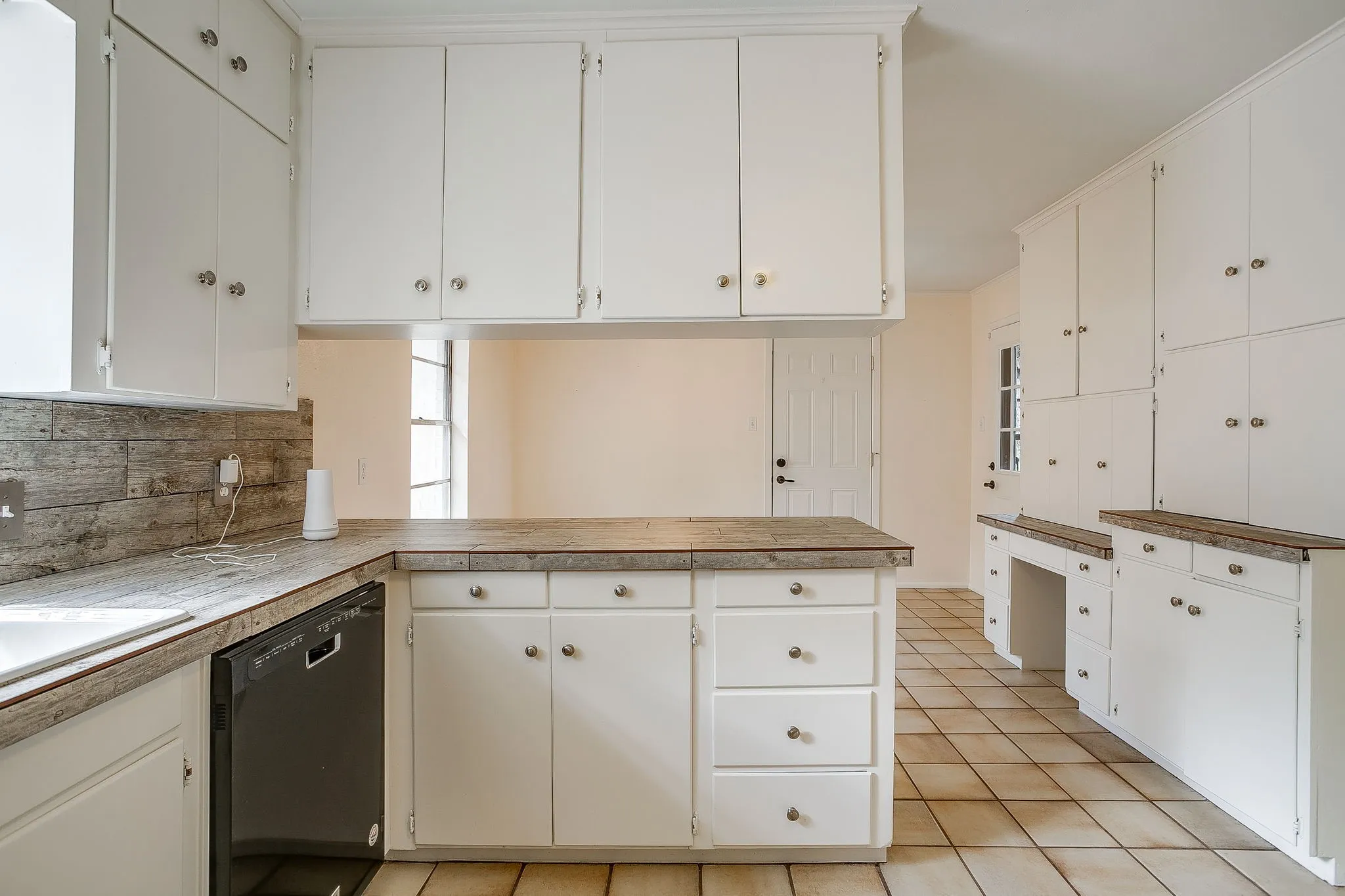 White cabinetry with silver-tone hardware, wood-finish countertops, tile backsplash, and integrated dishwasher