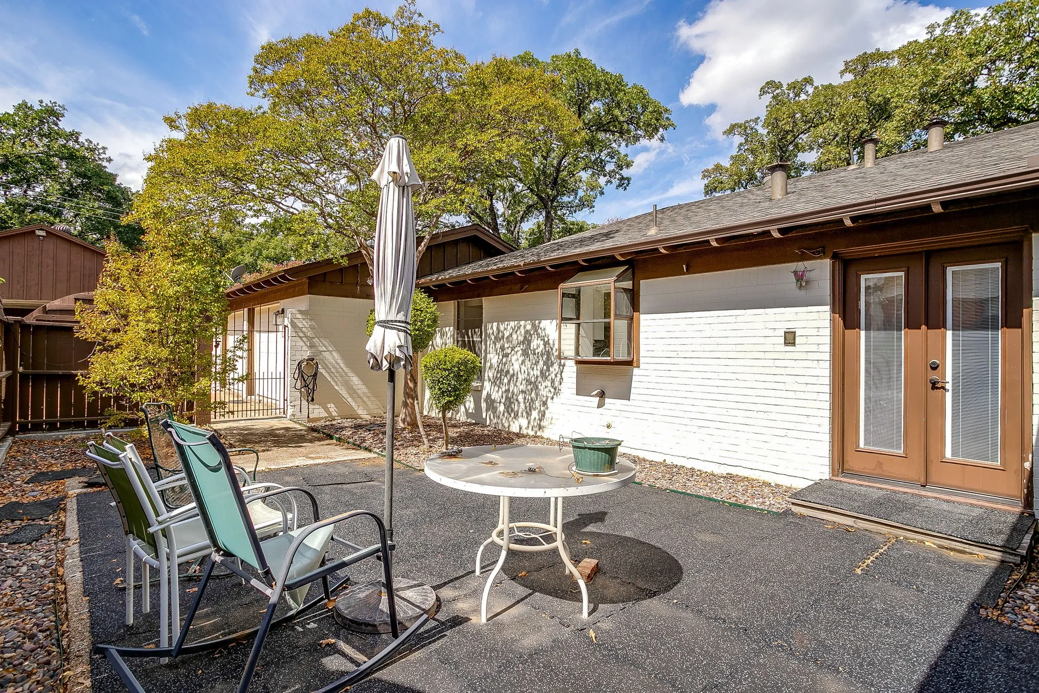 Paved patio area, white brick exterior, brown trim, double glass-paneled entry doors, and a bay window