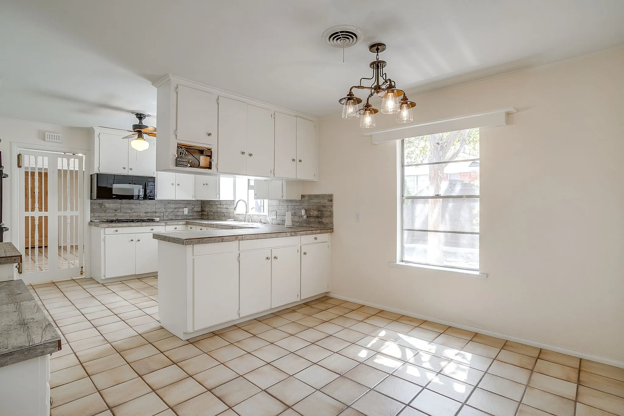 Kitchen featuring white cabinetry, tile backsplash, built-in microwave, U-shaped counter space, and tile flooring