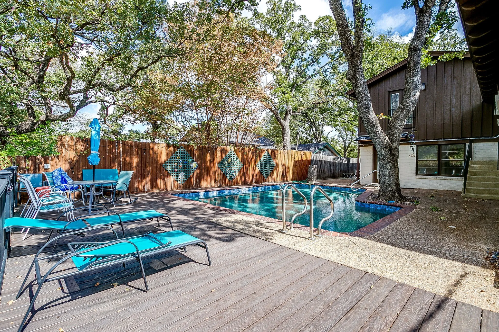 Expansive wood-finish deck with an in-ground swimming pool, surrounded by a wood privacy fence and mature trees