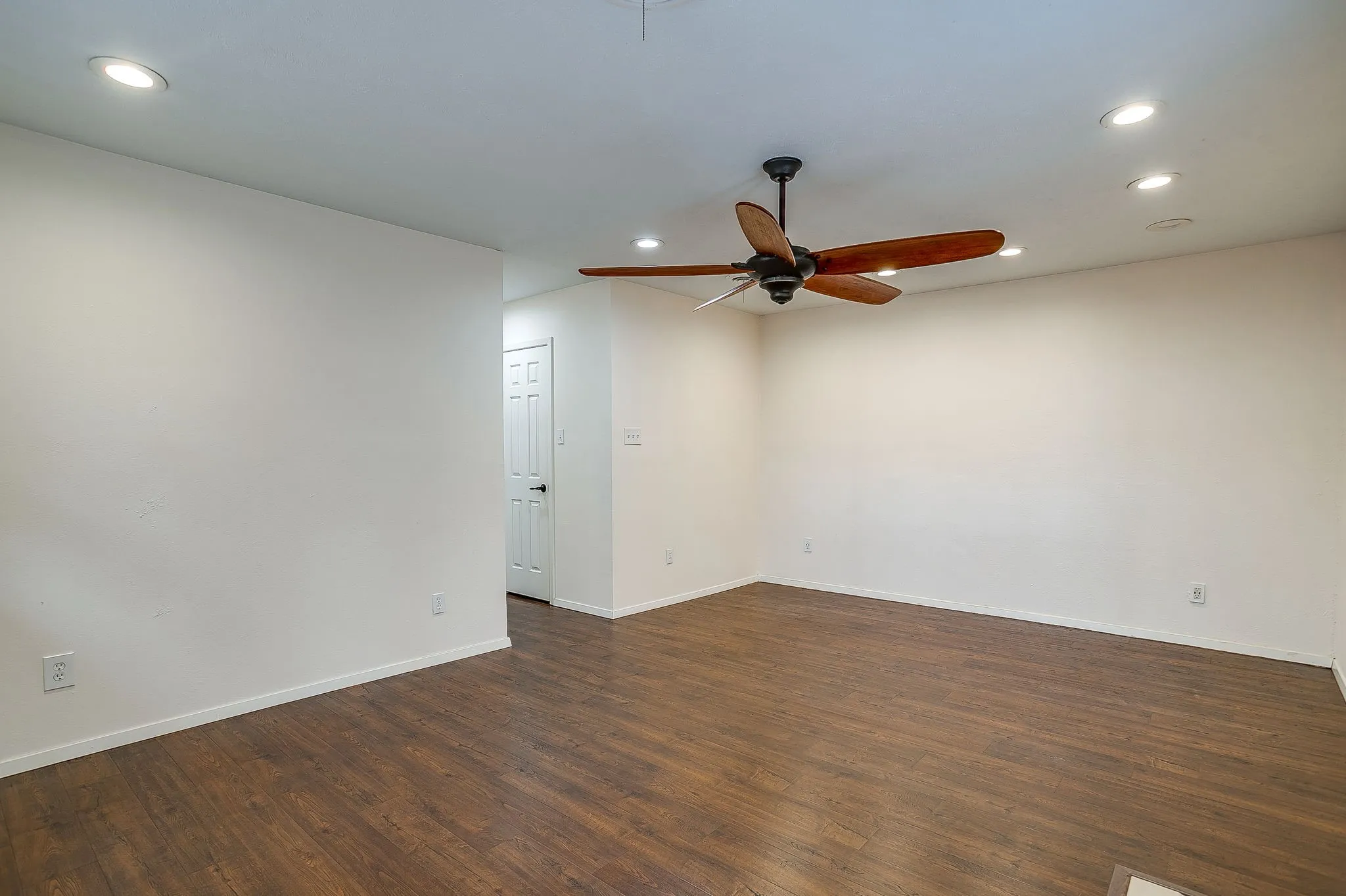 Wood-finish flooring, recessed lighting, ceiling fan with wood-look blades, white paneled interior door, and white walls