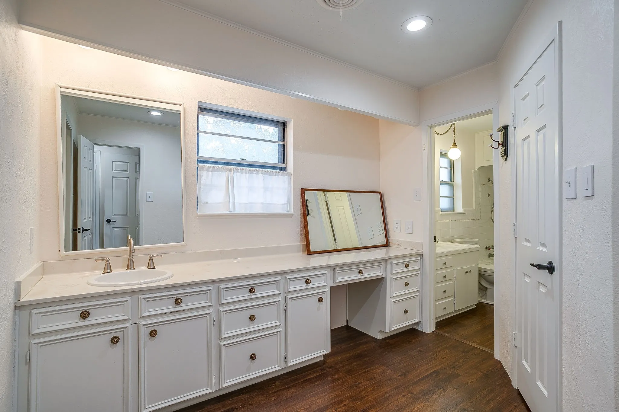 Expansive vanity with integrated sink and brass-finish faucet, ample storage cabinetry, and wood-finish flooring