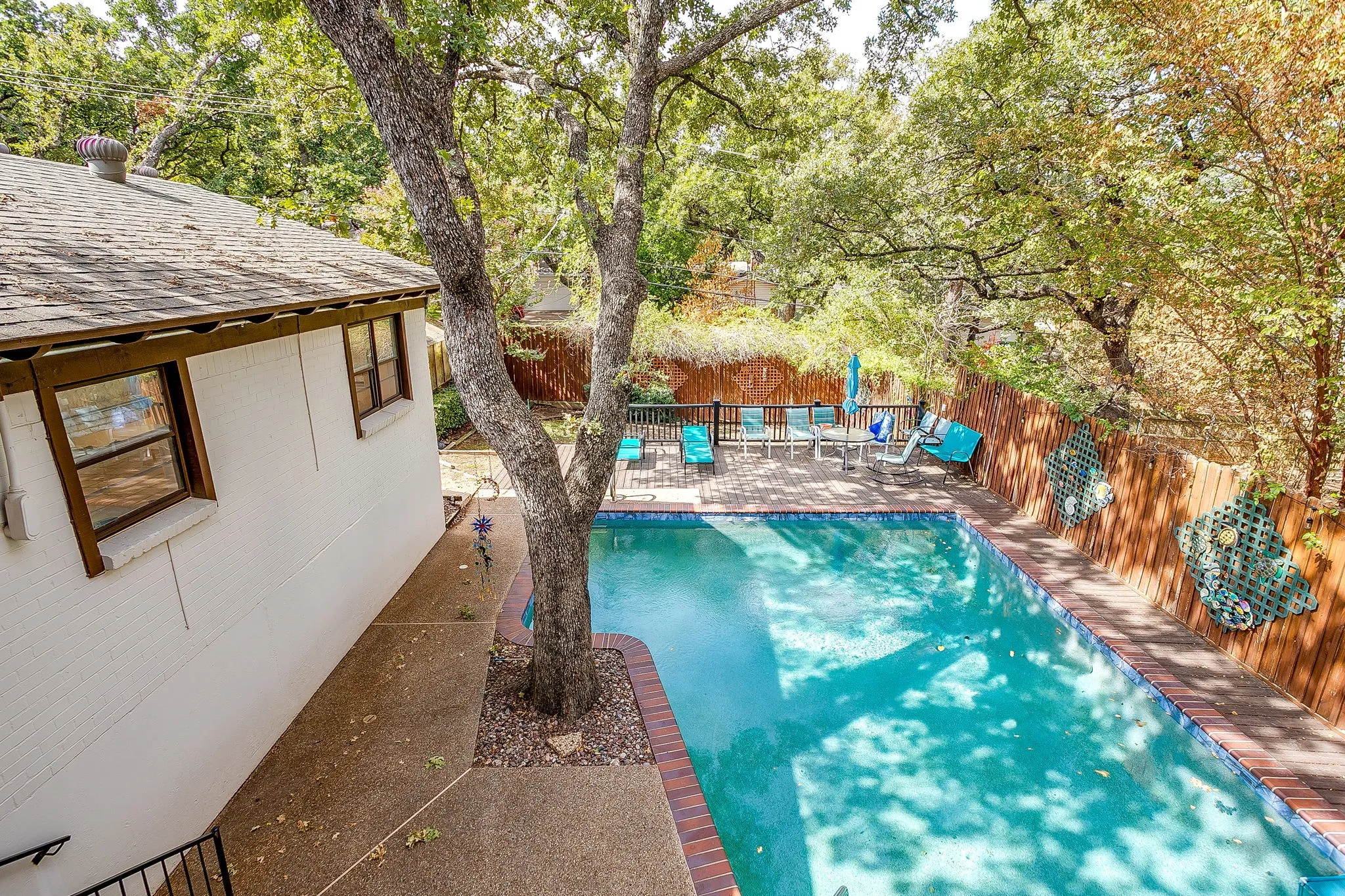 Rectangular swimming pool with brick coping, an adjacent paved patio, and a privacy fence