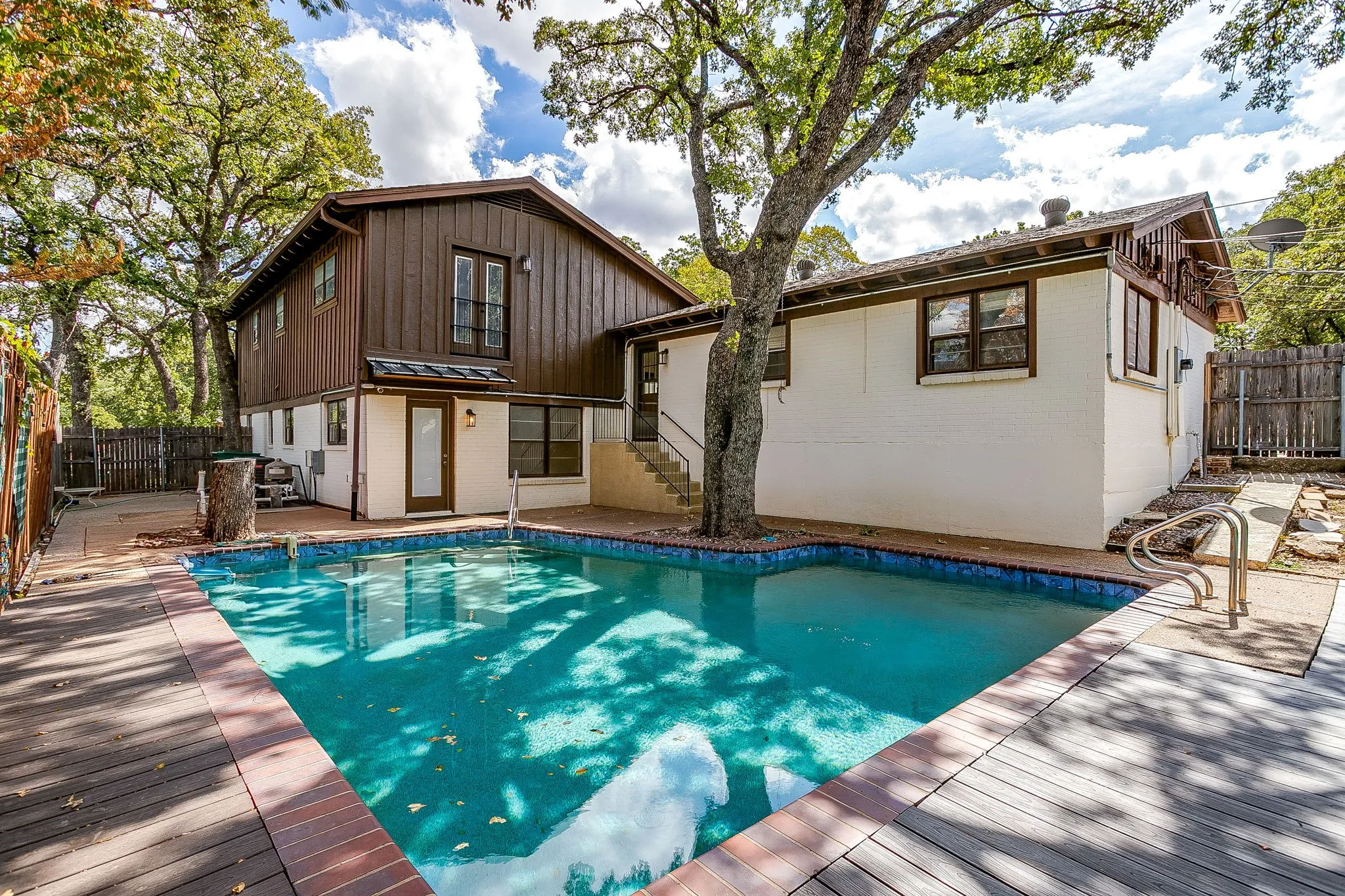 In-ground swimming pool with a surrounding wood-finish deck and brick trim