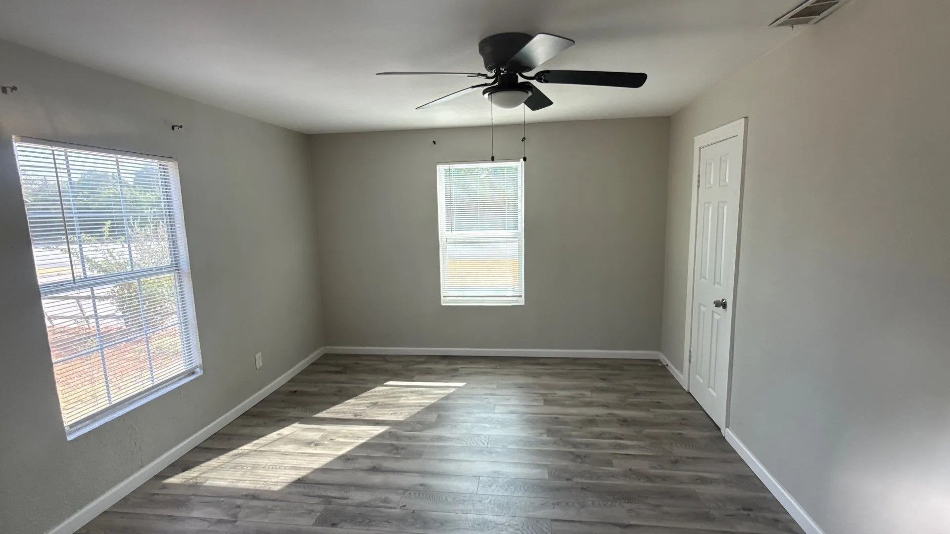 Wood-finish flooring, ceiling fan with integrated lighting, two windows with blinds, and a paneled interior door