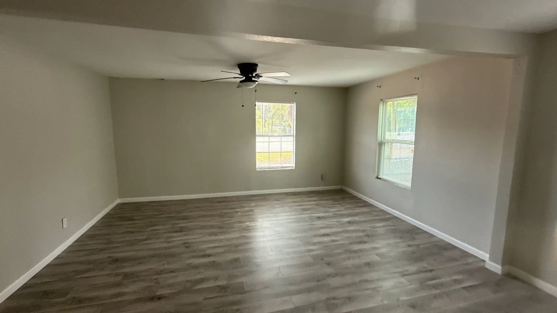 Spacious room featuring wood-finish flooring, neutral wall tones, two windows, and a ceiling fan