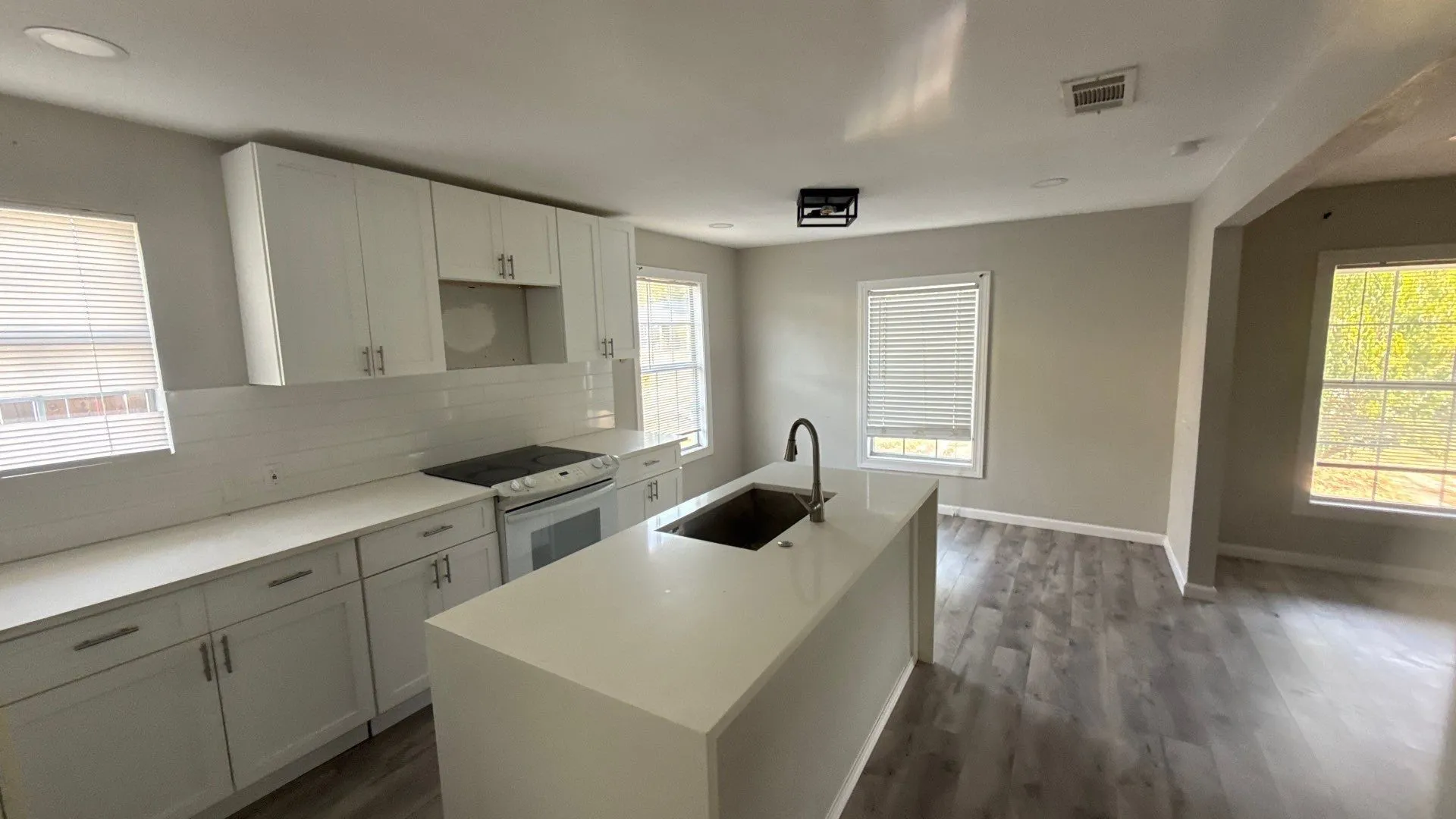 Modern kitchen featuring white cabinetry, a large center island with an integrated sink, a white subway tile backsplash, and sleek wood-finish flooring