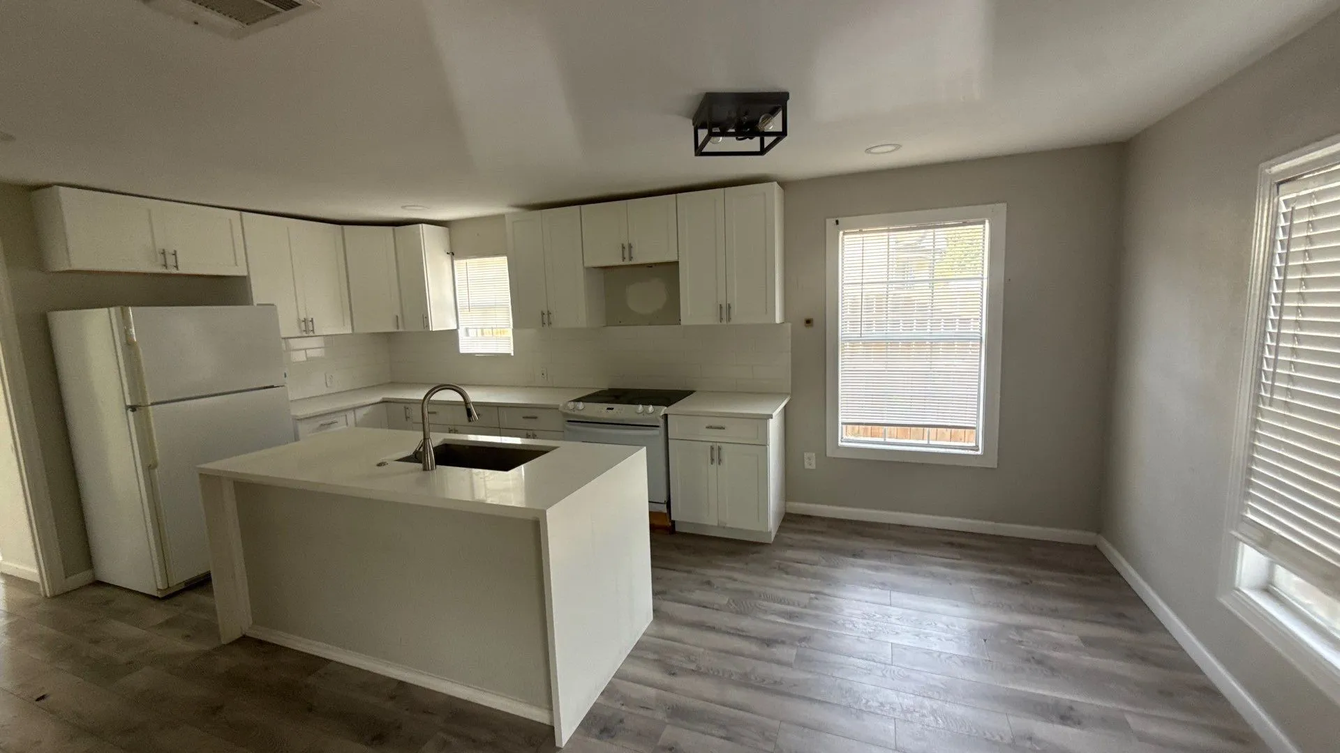 Modern kitchen featuring white cabinetry, stainless steel appliances, a large center island with undermount sink, wood-finish flooring, and abundant natural light from multiple windows