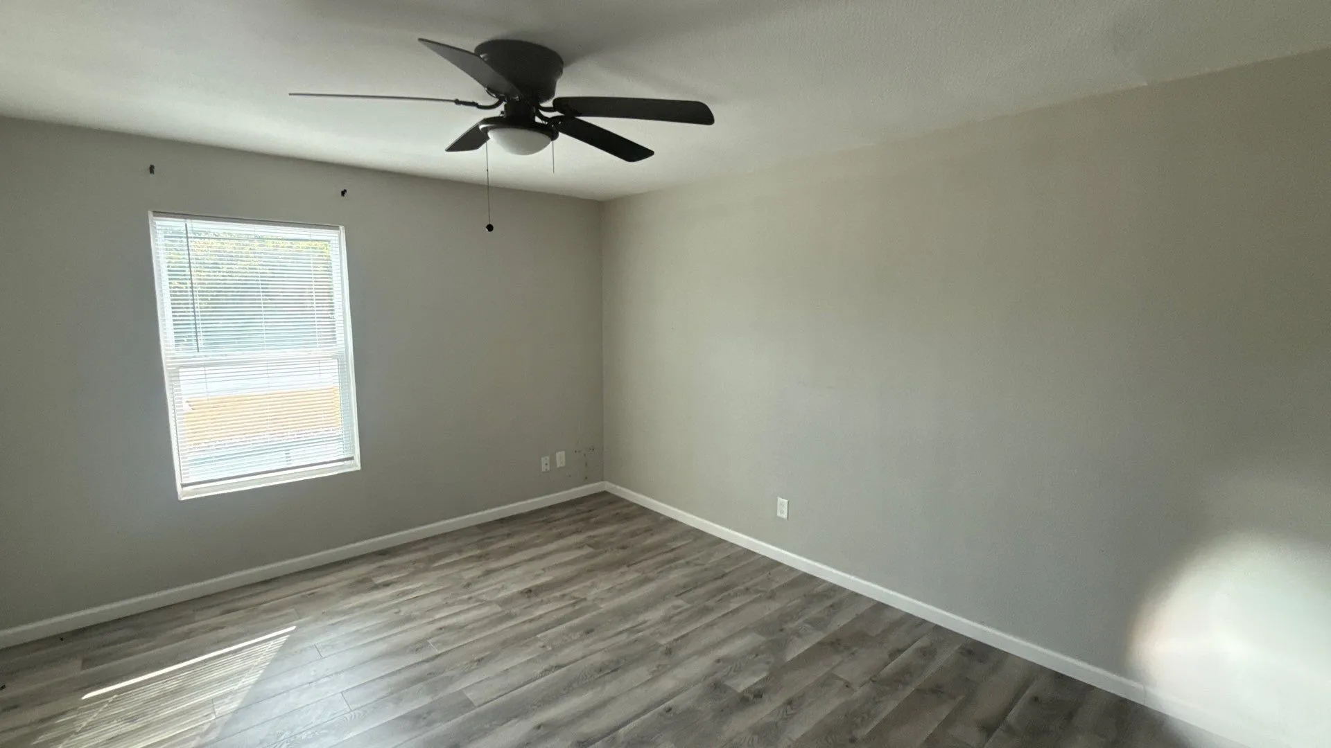 Wood-finish flooring, single window, ceiling fan with integrated lighting, and neutral wall tones