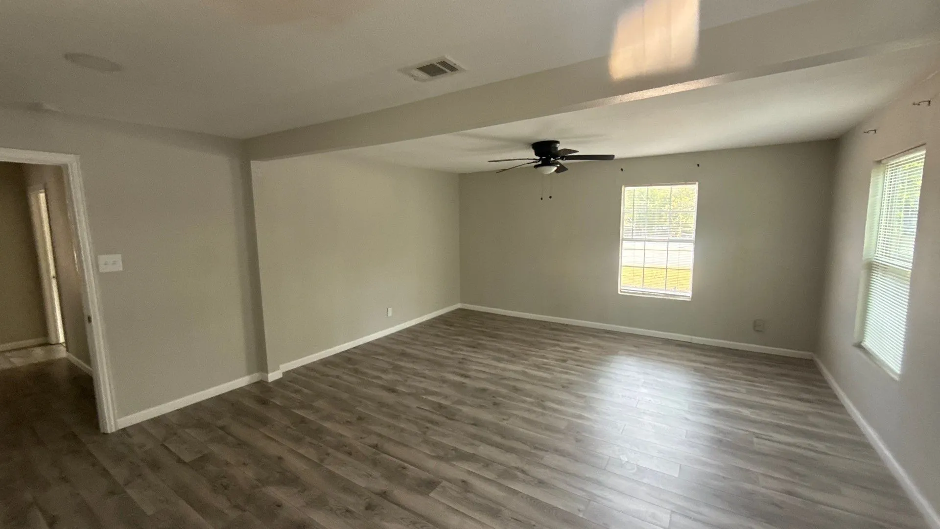 Wood-finish flooring, neutral wall tones, ceiling fan, and multiple windows with blinds