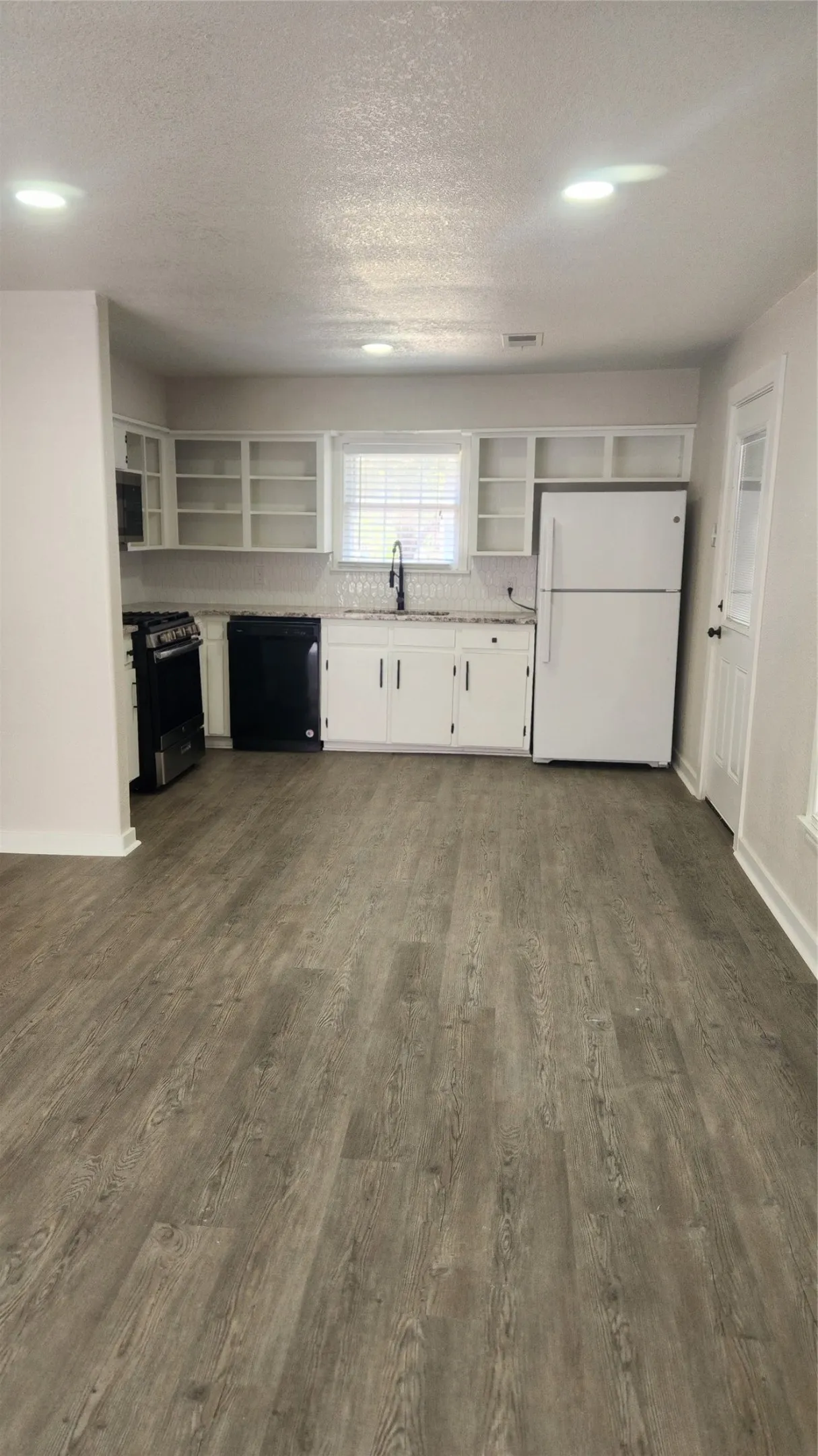 Open-concept kitchen with wood-finish flooring, white cabinetry, integrated appliances, and a tiled backsplash
