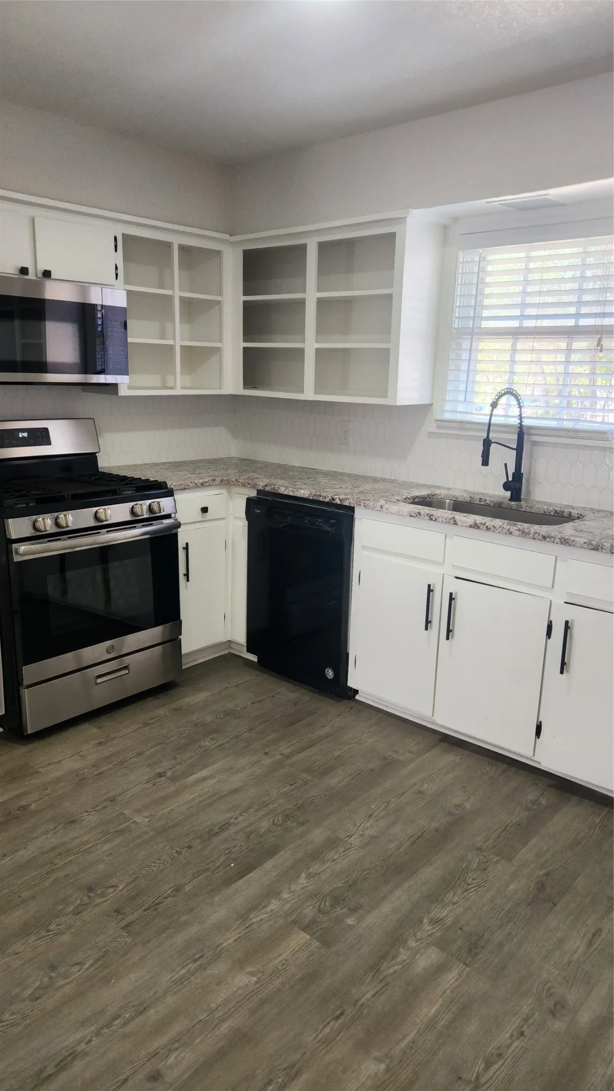Kitchen featuring wood-finish flooring, white cabinetry, speckled countertops, stainless steel appliances, and a window with blinds