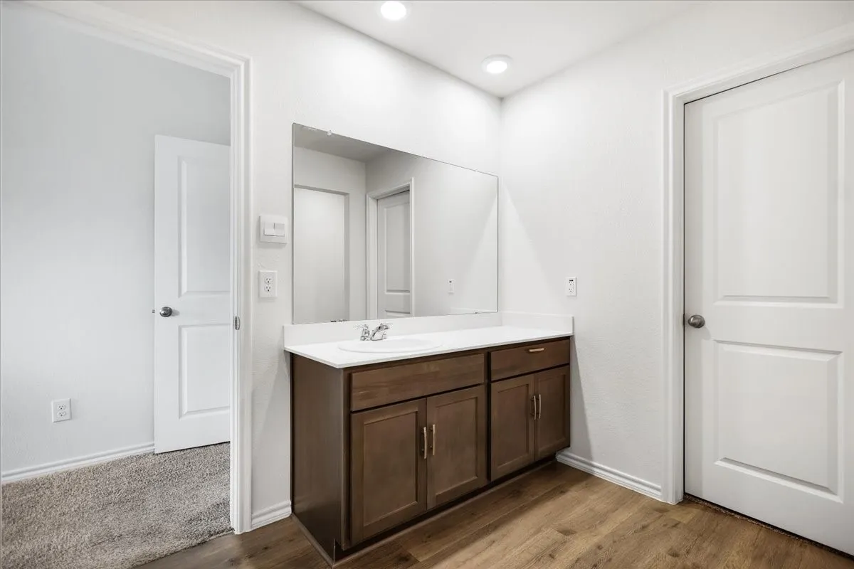 Vanity area featuring a wood-finish cabinet with brass hardware, white countertop, and an integrated sink