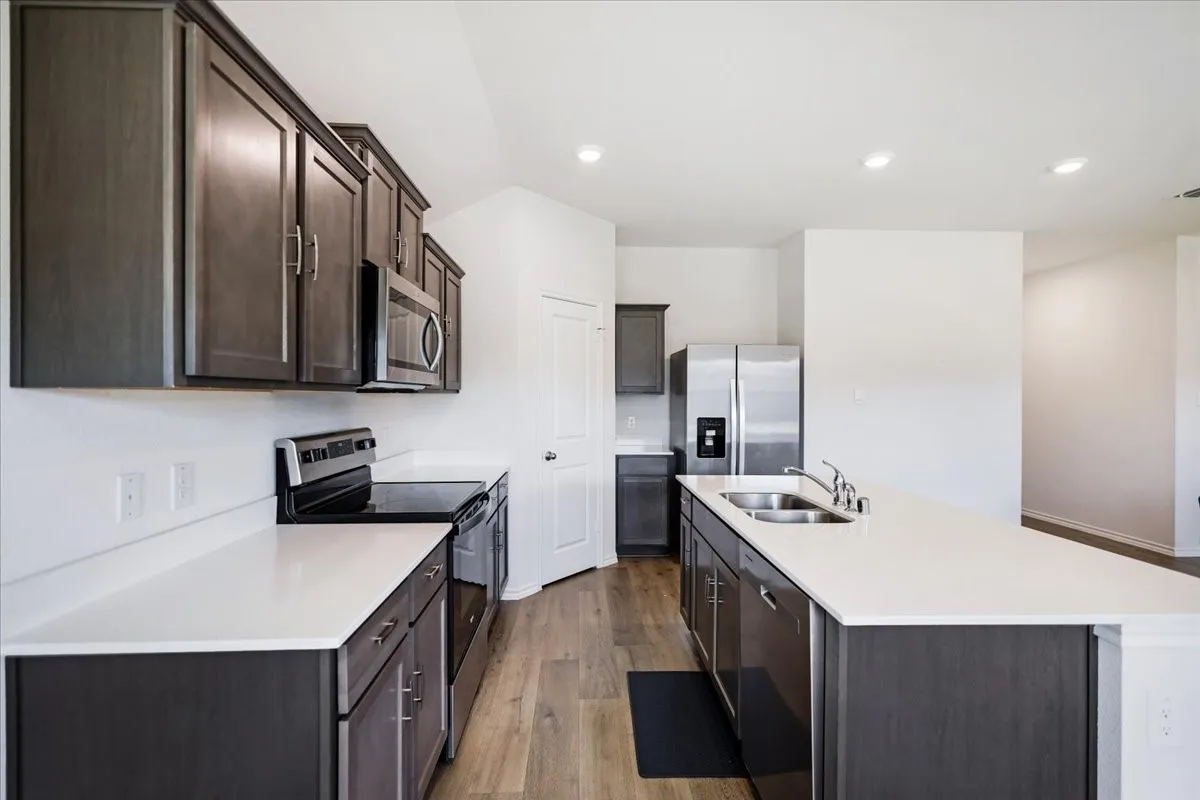 Kitchen featuring dark wood-finish cabinetry, light-toned countertops, stainless steel appliances, and wood-finish flooring