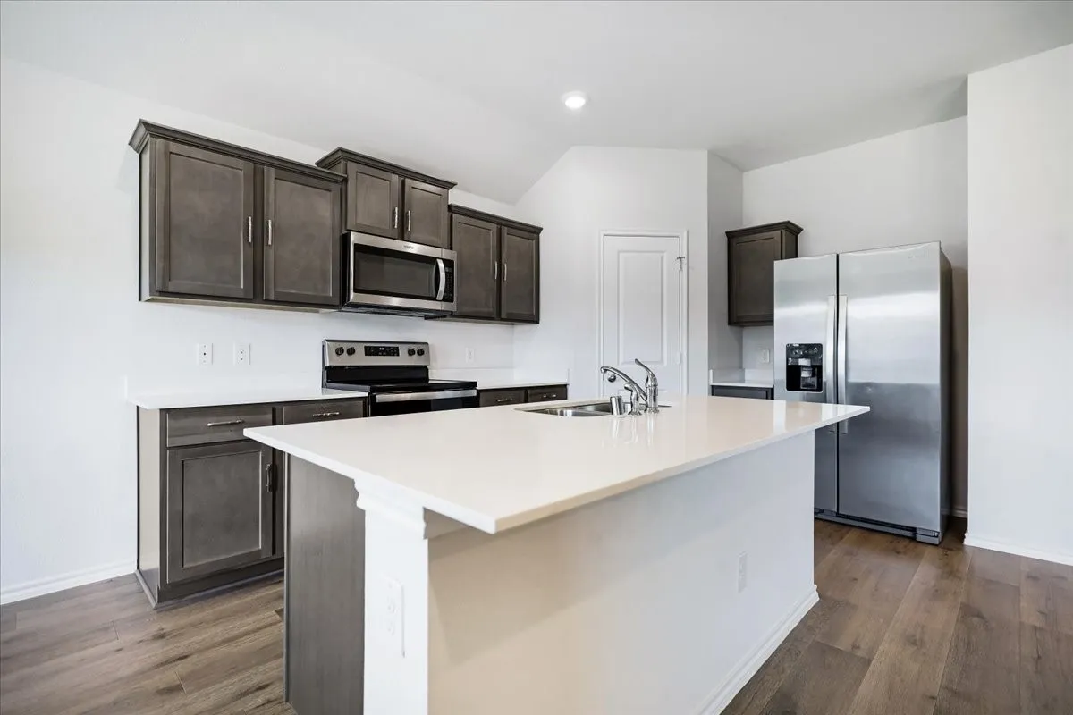 Modern kitchen featuring a central island, stainless steel appliances, dark wood-finish cabinetry, light countertops, and wood-finish flooring