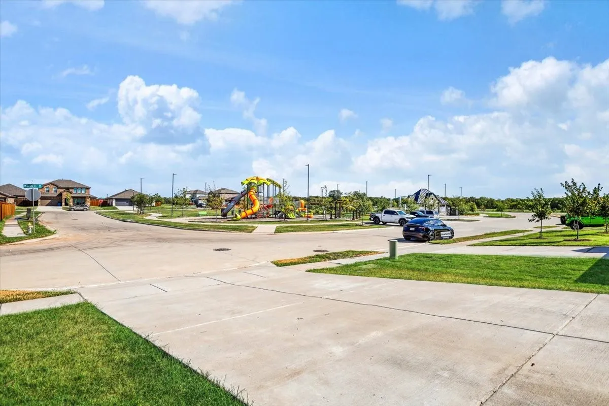 Neighborhood greenspace featuring a playground with colorful equipment, paved pathways, and street lighting