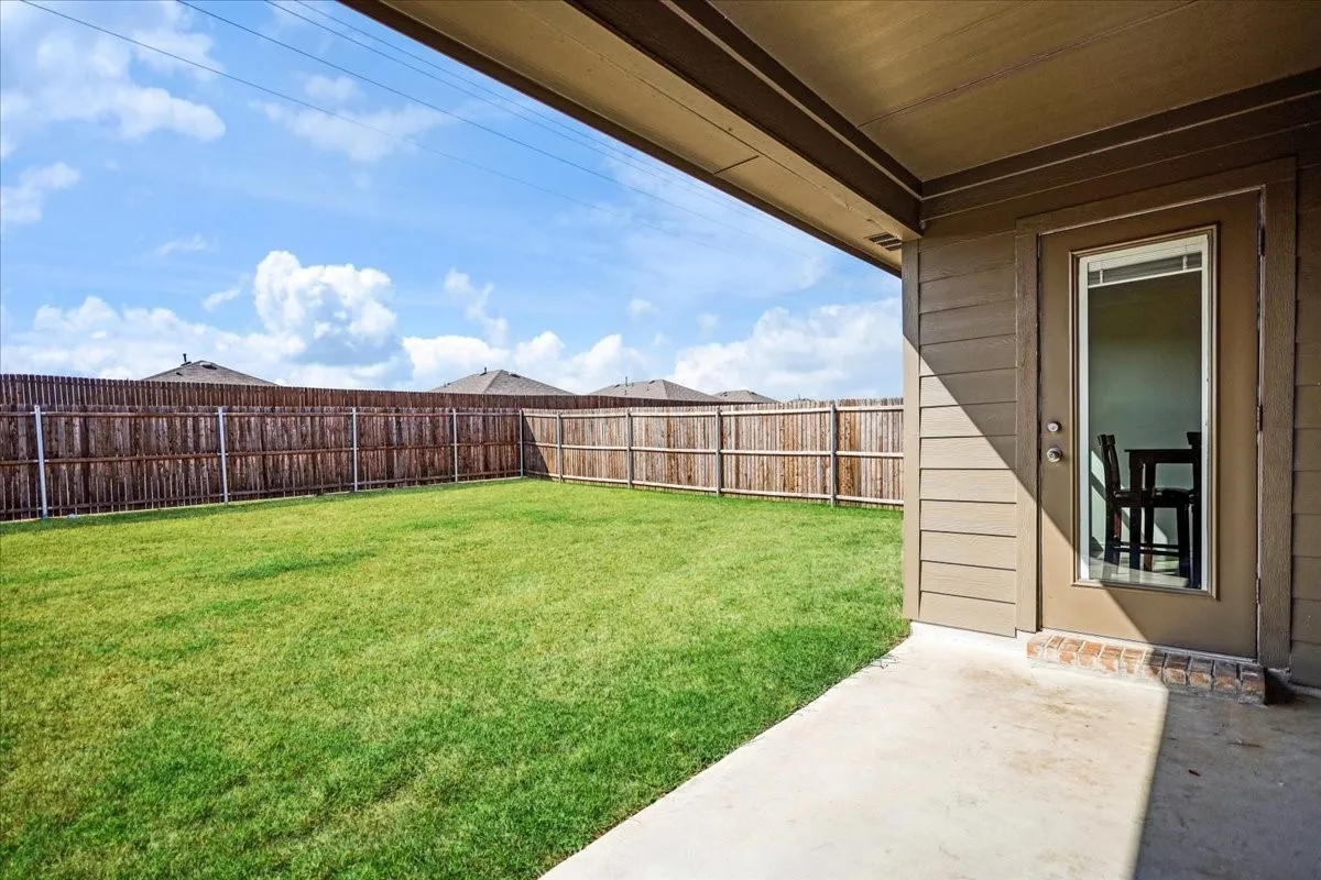 Expansive grassy yard with a wood privacy fence, covered patio, and exterior siding