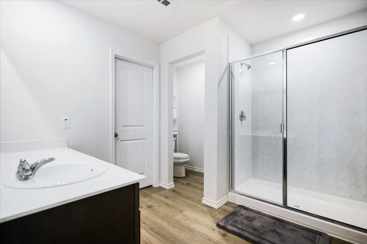 Bathroom featuring a glass-enclosed shower, wood-finish flooring, a vanity with a white countertop, and a built-in sink