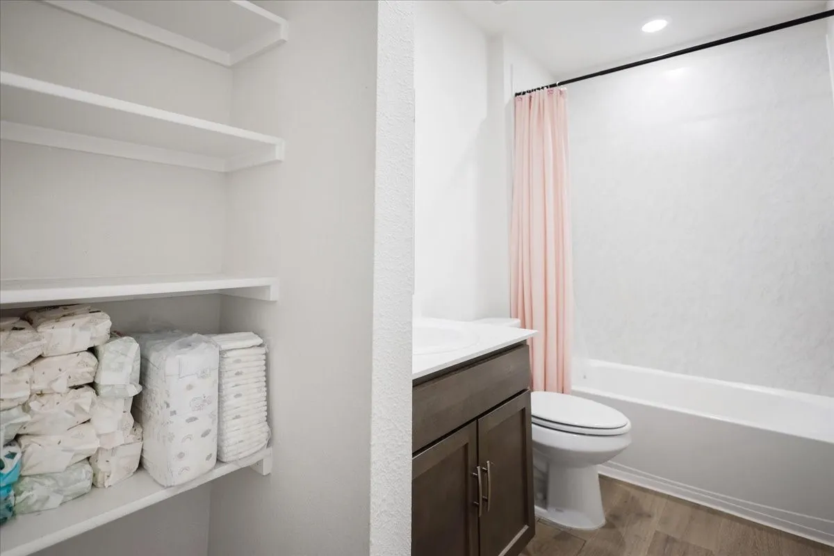 Integrated storage shelves, wood-finish flooring, single vanity with integrated sink, white bathtub with shower, and recessed lighting