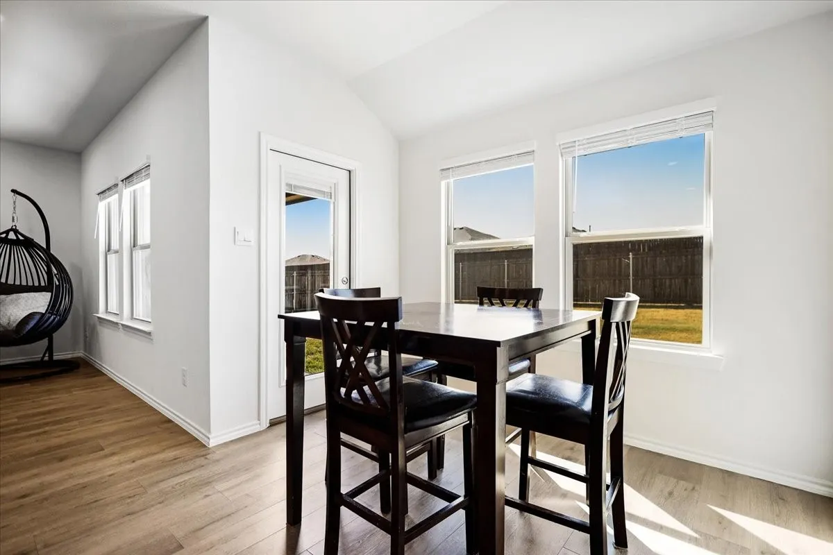 Vaulted ceiling, wood-finish flooring, white walls, multiple windows, and a glass-paneled door