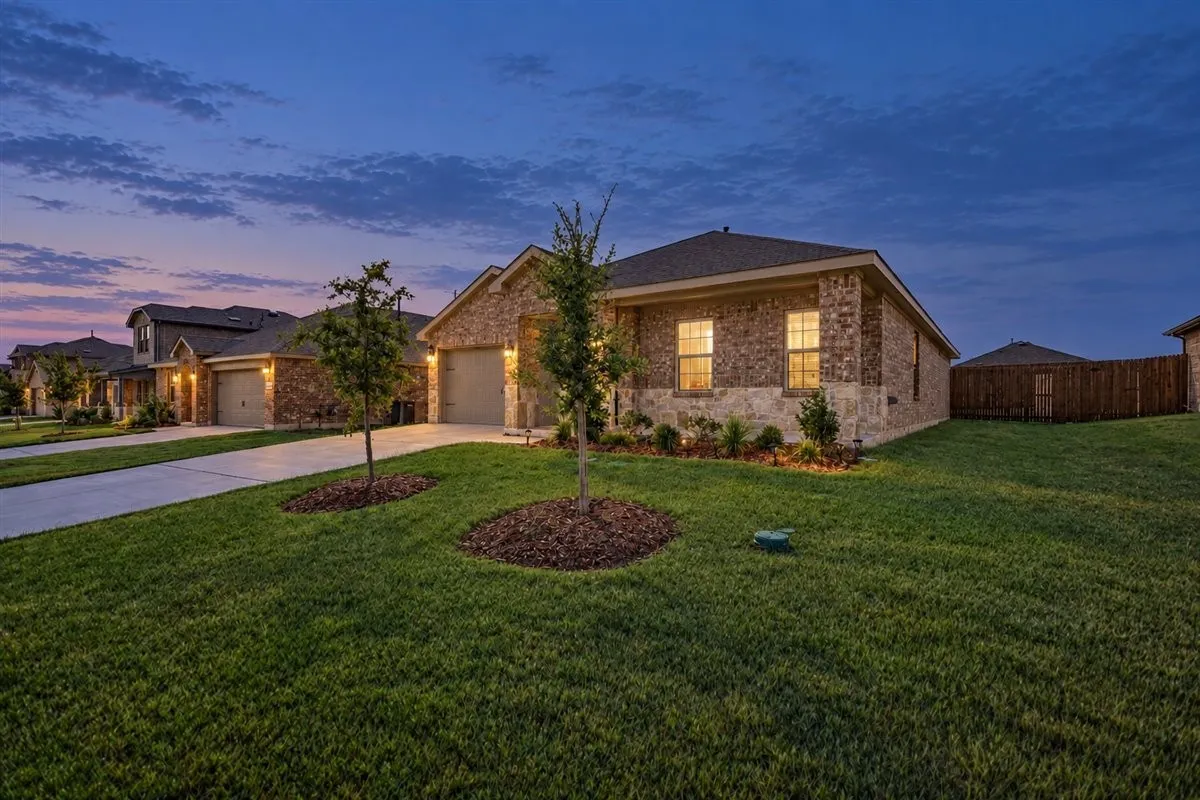 Brick and stone facade, attached garage, well-maintained lawn, privacy fencing, and concrete driveway