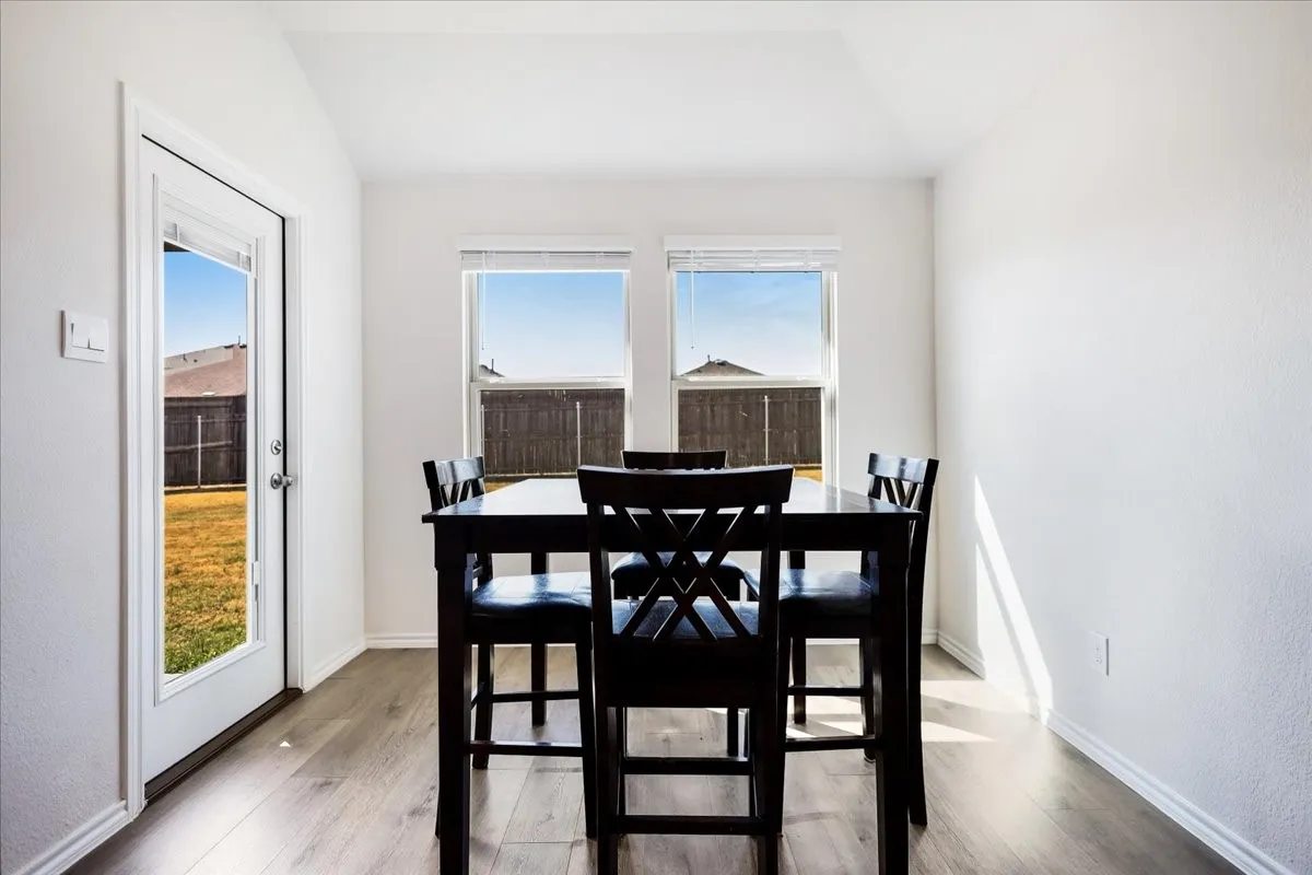 Vaulted ceiling, two windows with blinds, wood-finish flooring, white walls, and a glass-paneled door