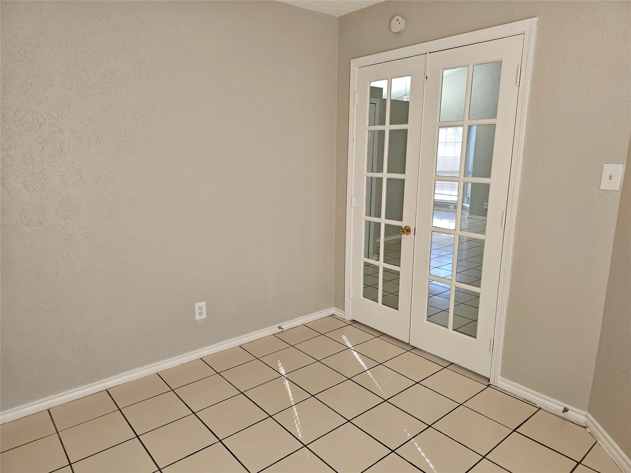 Double French doors with glass panels, light-toned tile flooring, and neutral wall paint