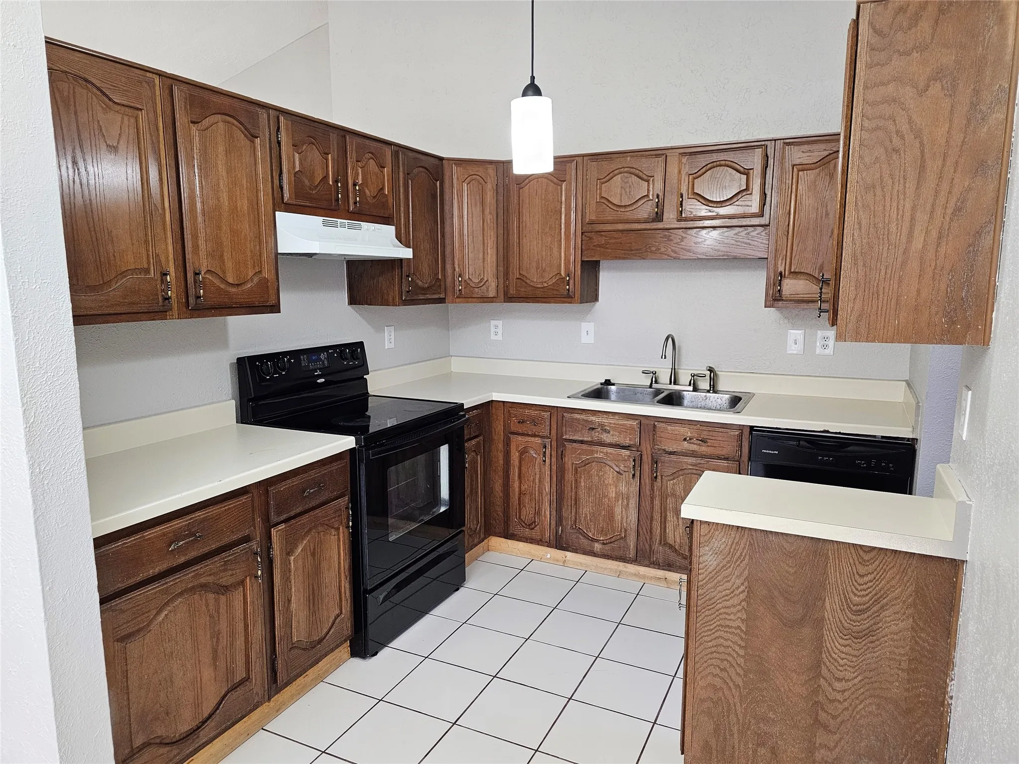 Kitchen featuring wood cabinetry, white countertops, dual basin sink with chrome faucet, black electric range, and white tiled flooring