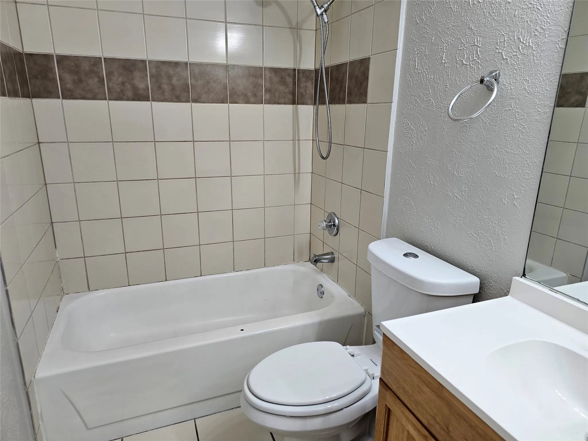 White bathtub with tile surround, integrated shower fixture, and a vanity with a white countertop and basin sink
