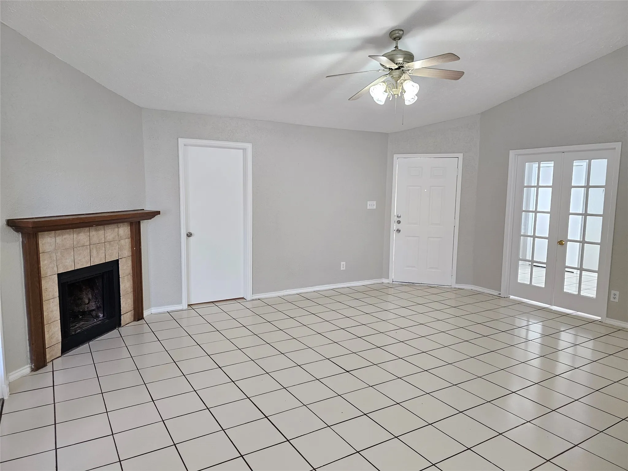 Tile flooring, corner fireplace with tile surround, wood mantel, ceiling fan with light fixture, and French doors