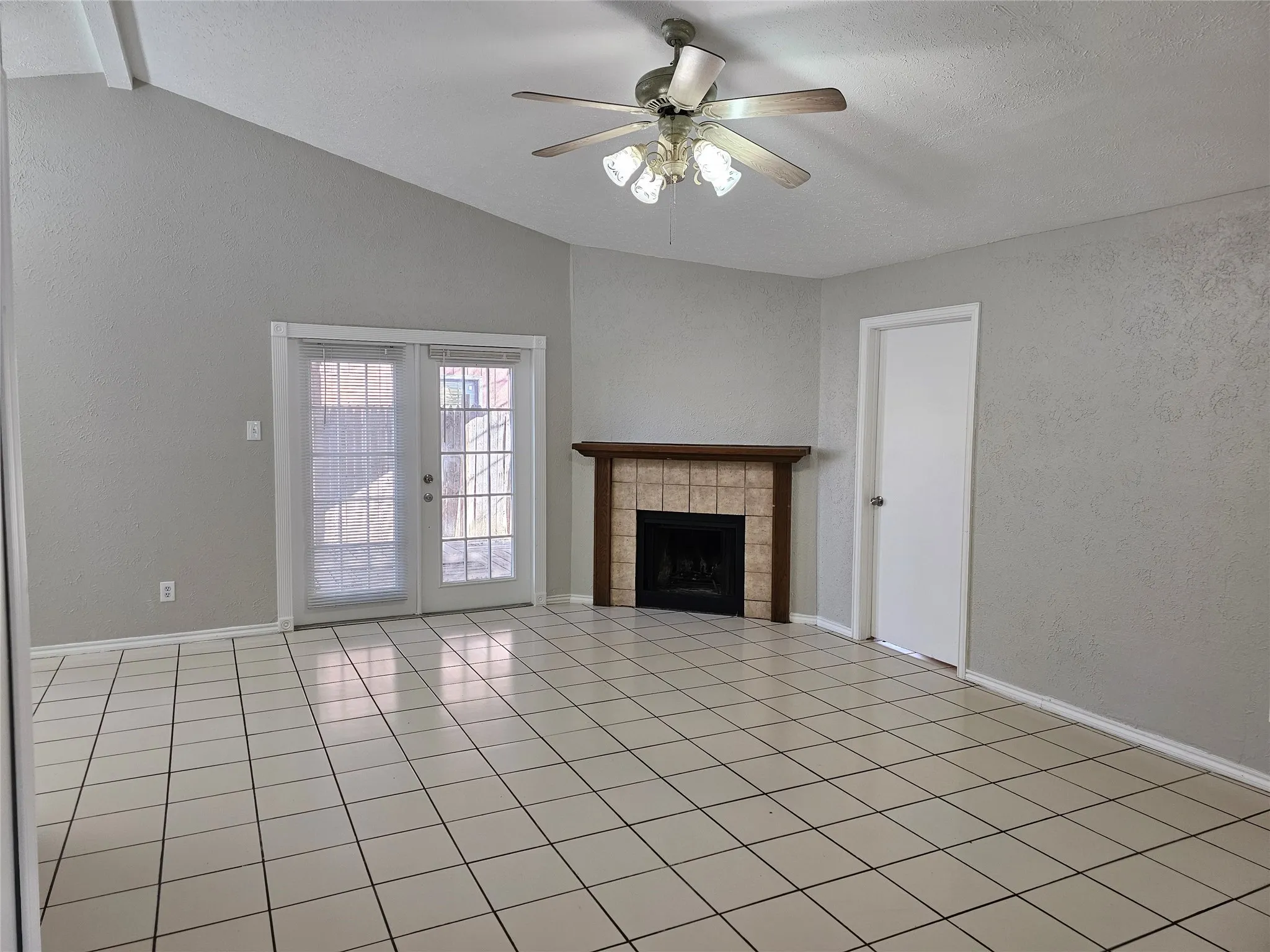 Vaulted ceiling with exposed beams, tile flooring, corner fireplace with a wood mantle, and double French doors with interior blinds