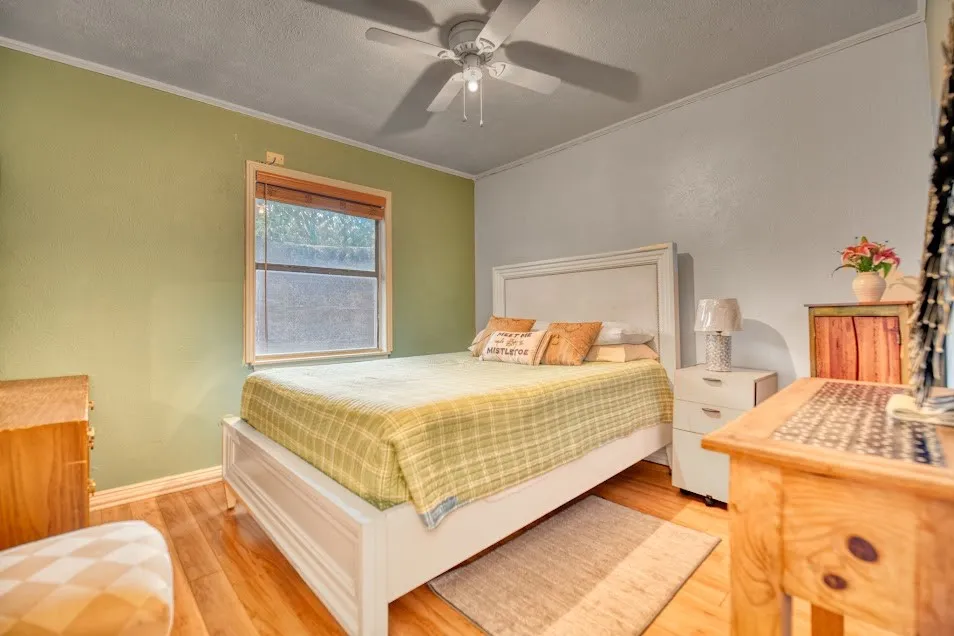 Hardwood-finish flooring, window with blinds, ceiling fan with light fixture, and crown molding