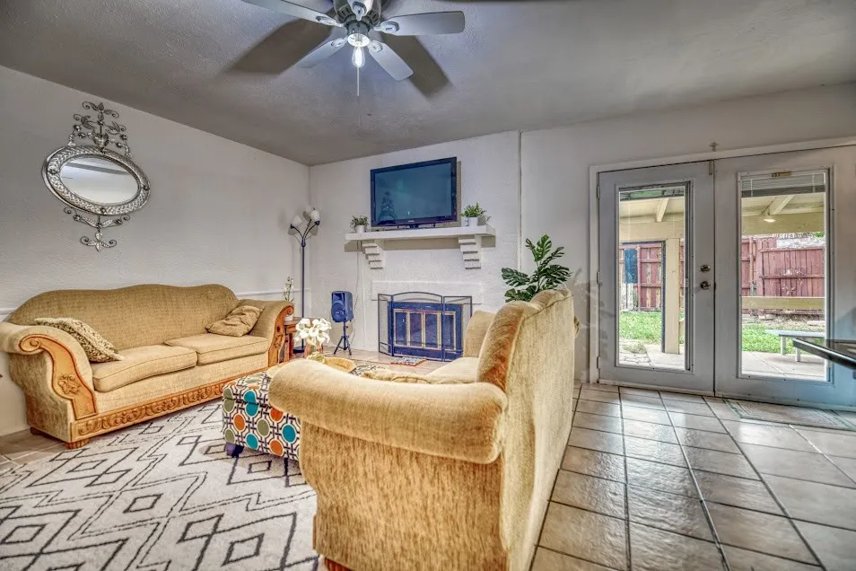 Ceramic tile flooring, white fireplace with mantle, double French doors, and ceiling fan with integrated lighting