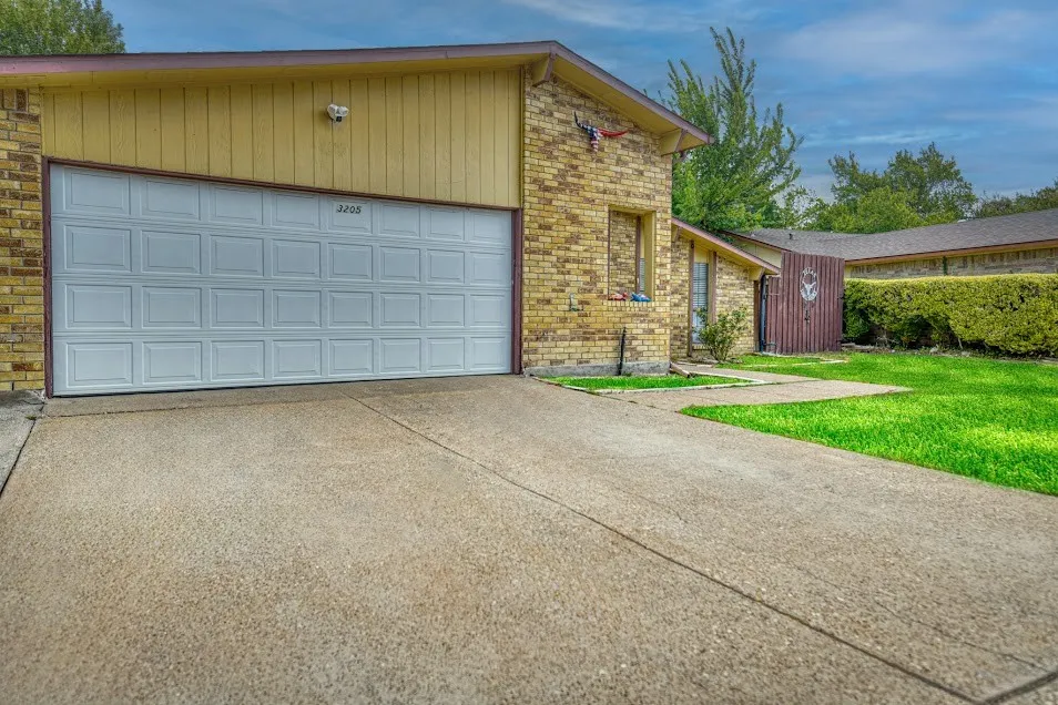 Brick exterior, paneled garage door, concrete driveway, manicured lawn, established shrubbery
