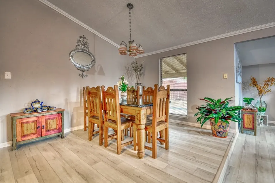 Crown molding and a chandelier illuminate the space, featuring light wood-finish flooring and a large window