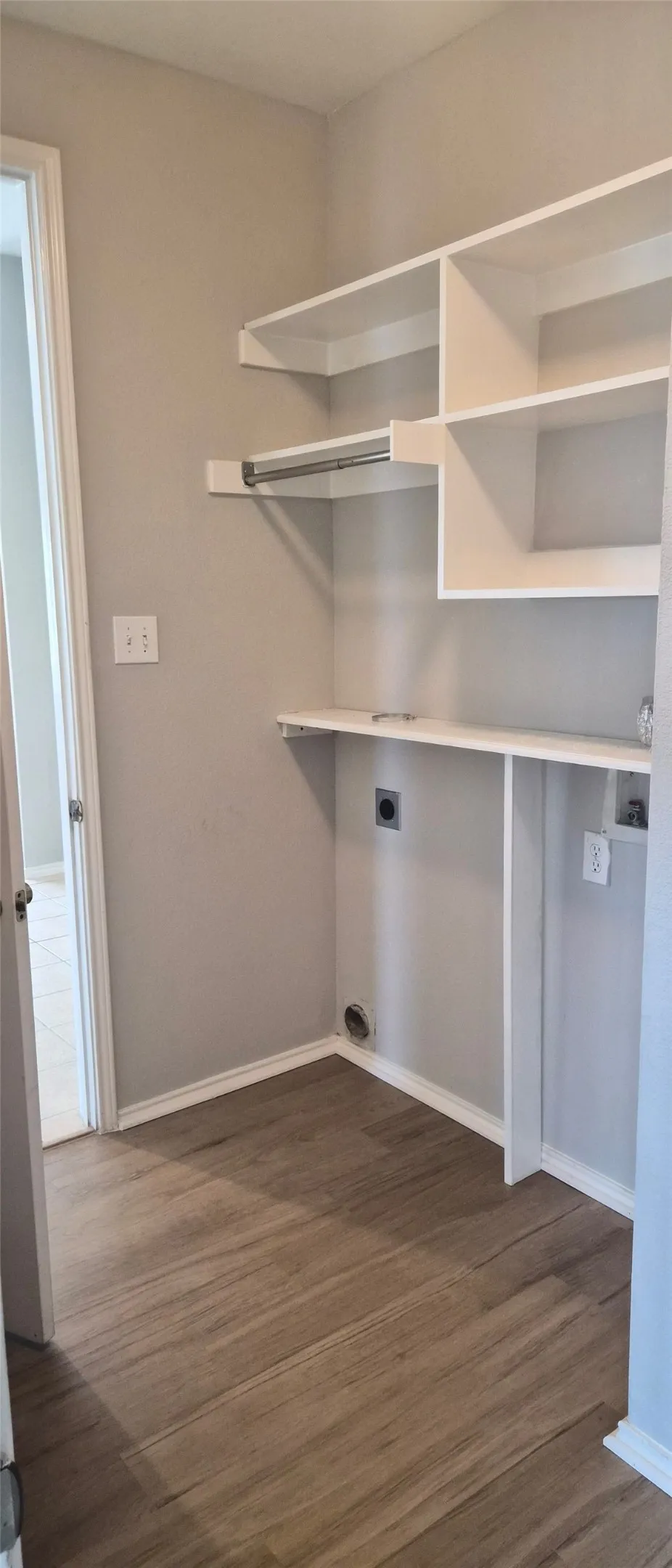 Utility space featuring wood-finish flooring, built-in shelving, and a hanging rod