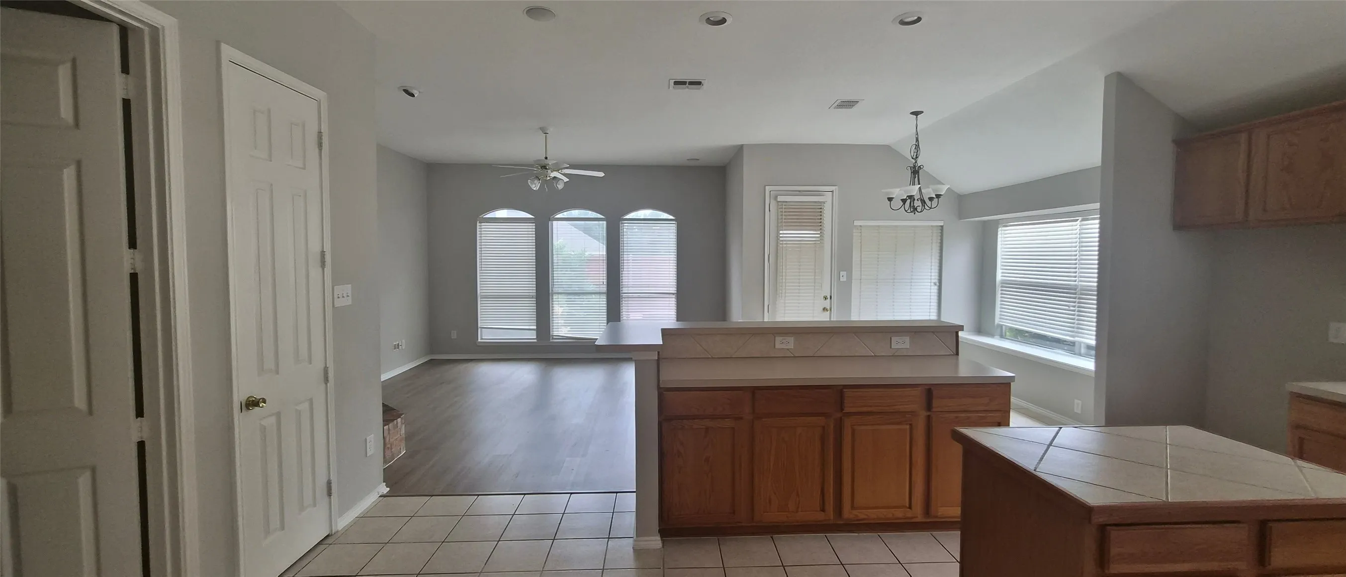 Open-concept layout with wood-finish flooring, vaulted ceilings, and a kitchen island with tile countertop