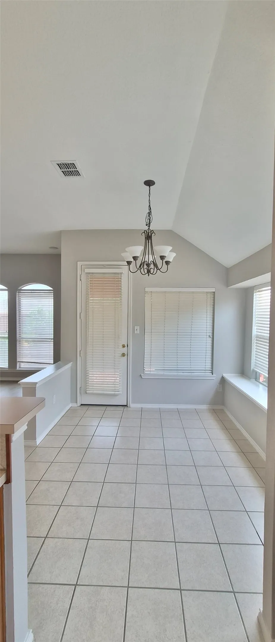 Vaulted ceiling, decorative chandelier, tiled flooring, built-in window seating, and a glass-paneled door
