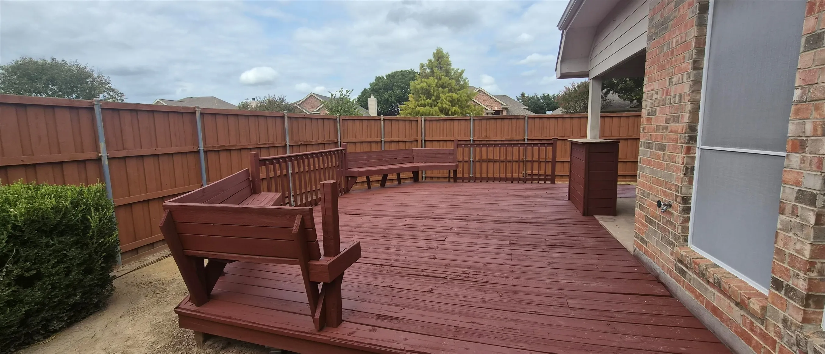 Expansive wood deck with built-in bench seating, privacy fencing, and brick exterior