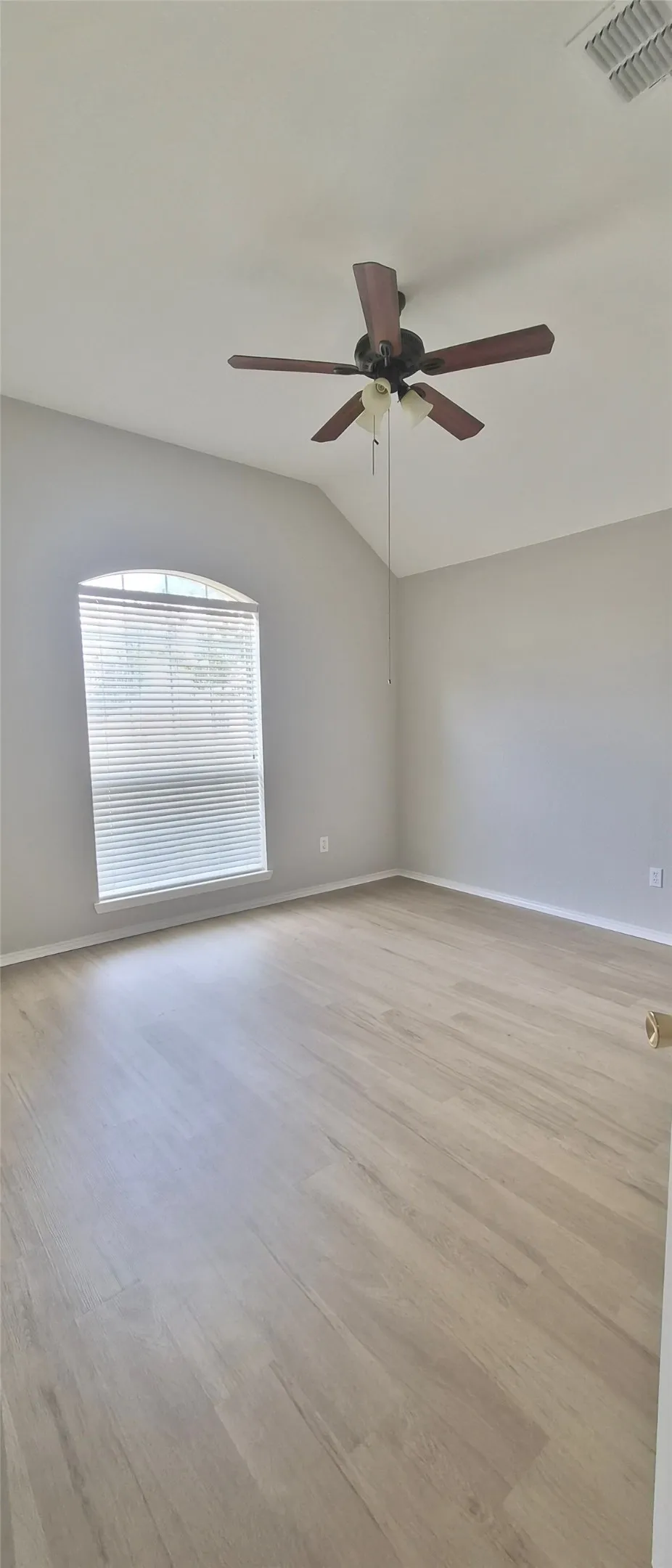 Vaulted ceiling, arched window with blinds, wood-finish flooring, and a ceiling fan with integrated lighting